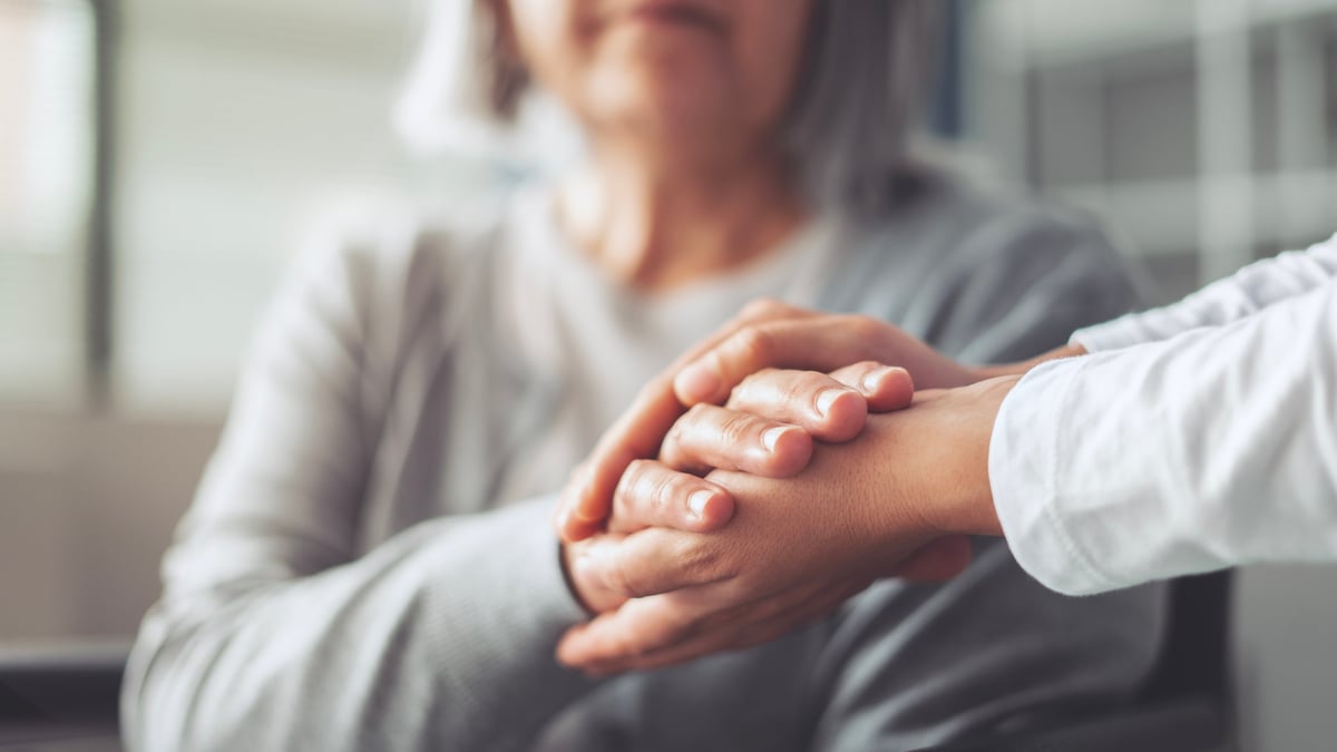 Hands holding an elderly woman's hands in comfort and care